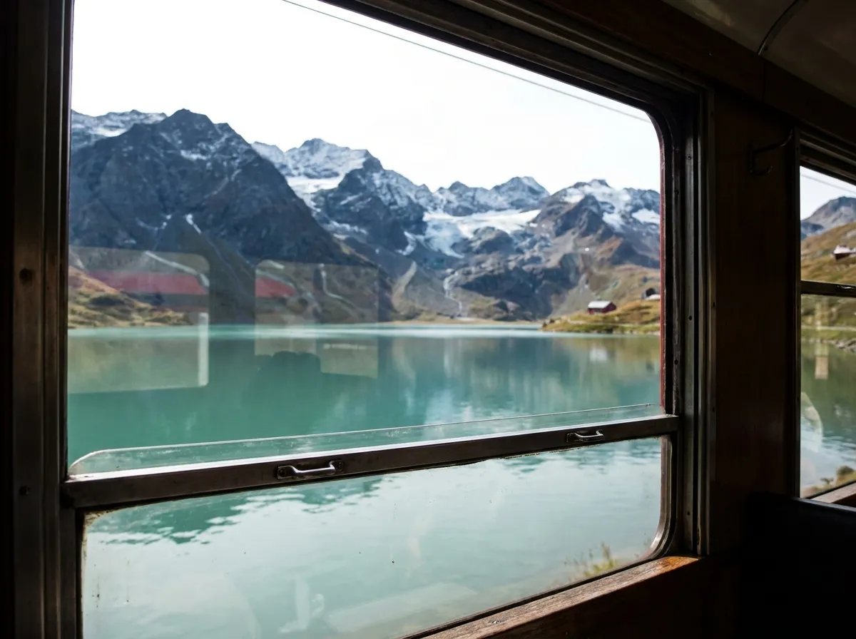 Turquoise alpine lake and snowy peaks seen through a train window